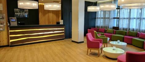 Un vestíbulo de hotel con mostrador de recepción, iluminación moderna y zonas de estar coloridas.