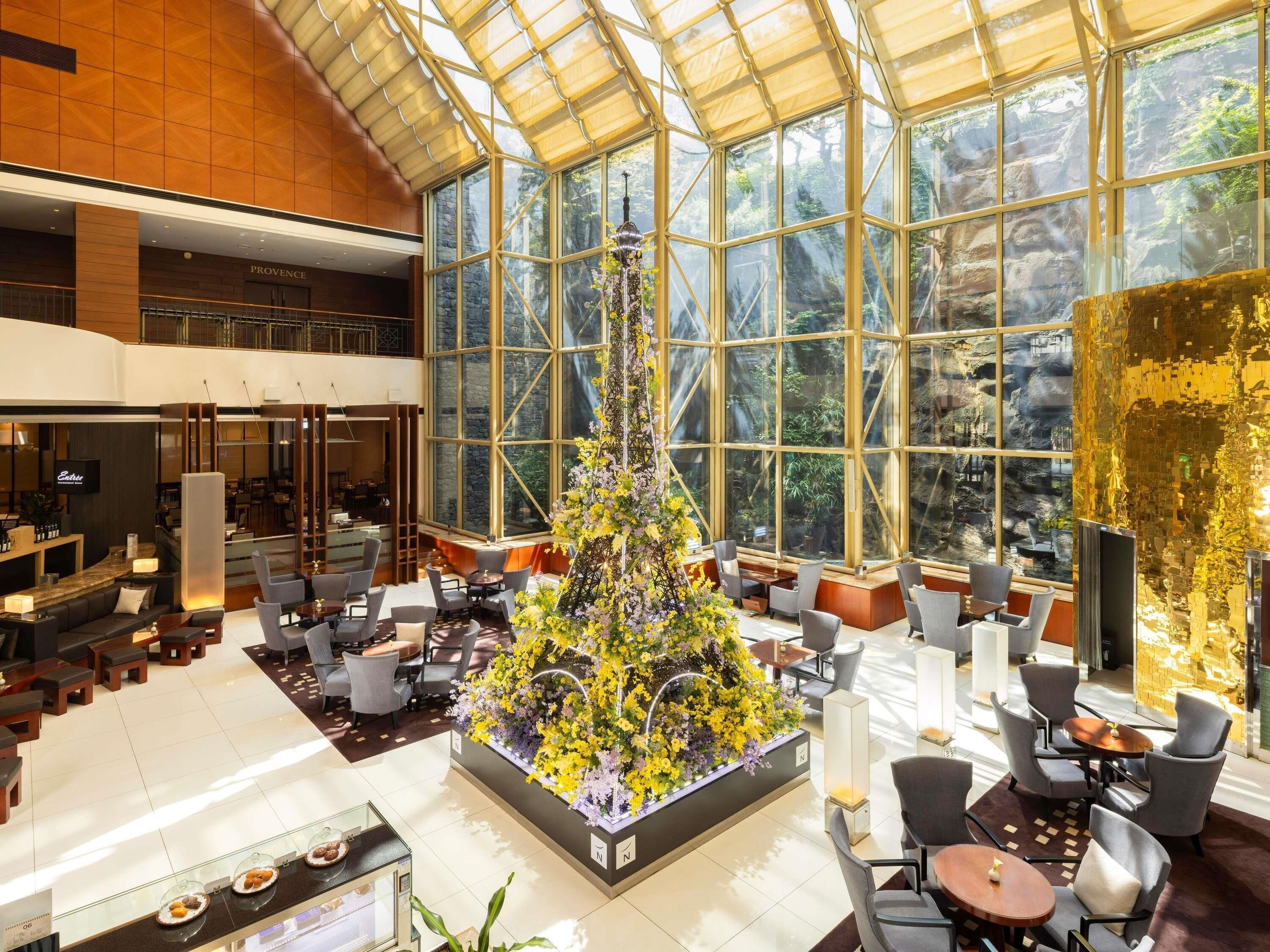 A spacious lobby with a large glass wall, a central floral arrangement, and a reception desk.