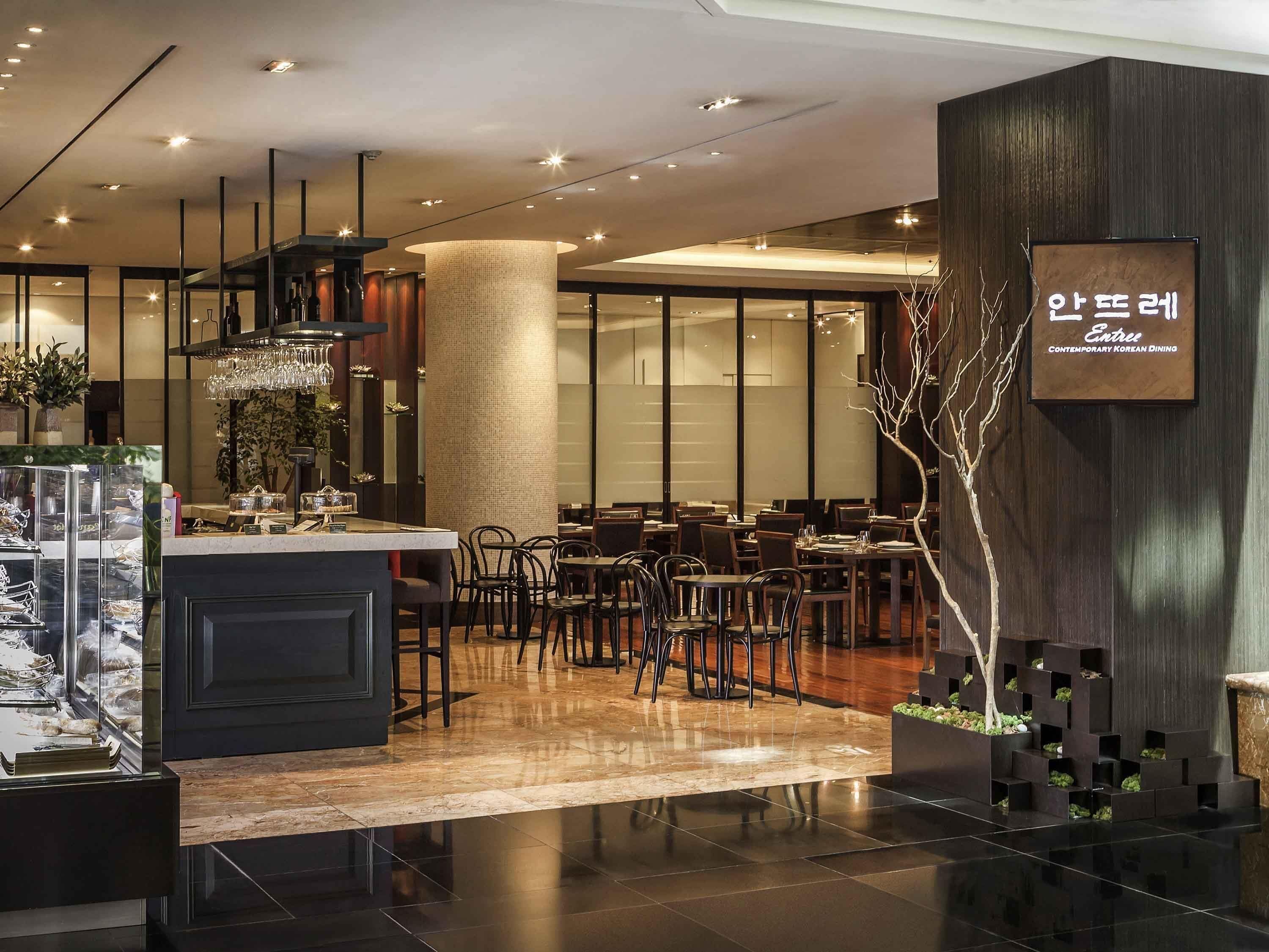 Un intérieur de restaurant moderne avec un îlot central, des tables et des chaises disposées de manière harmonieuse, et un arbre décoratif.
