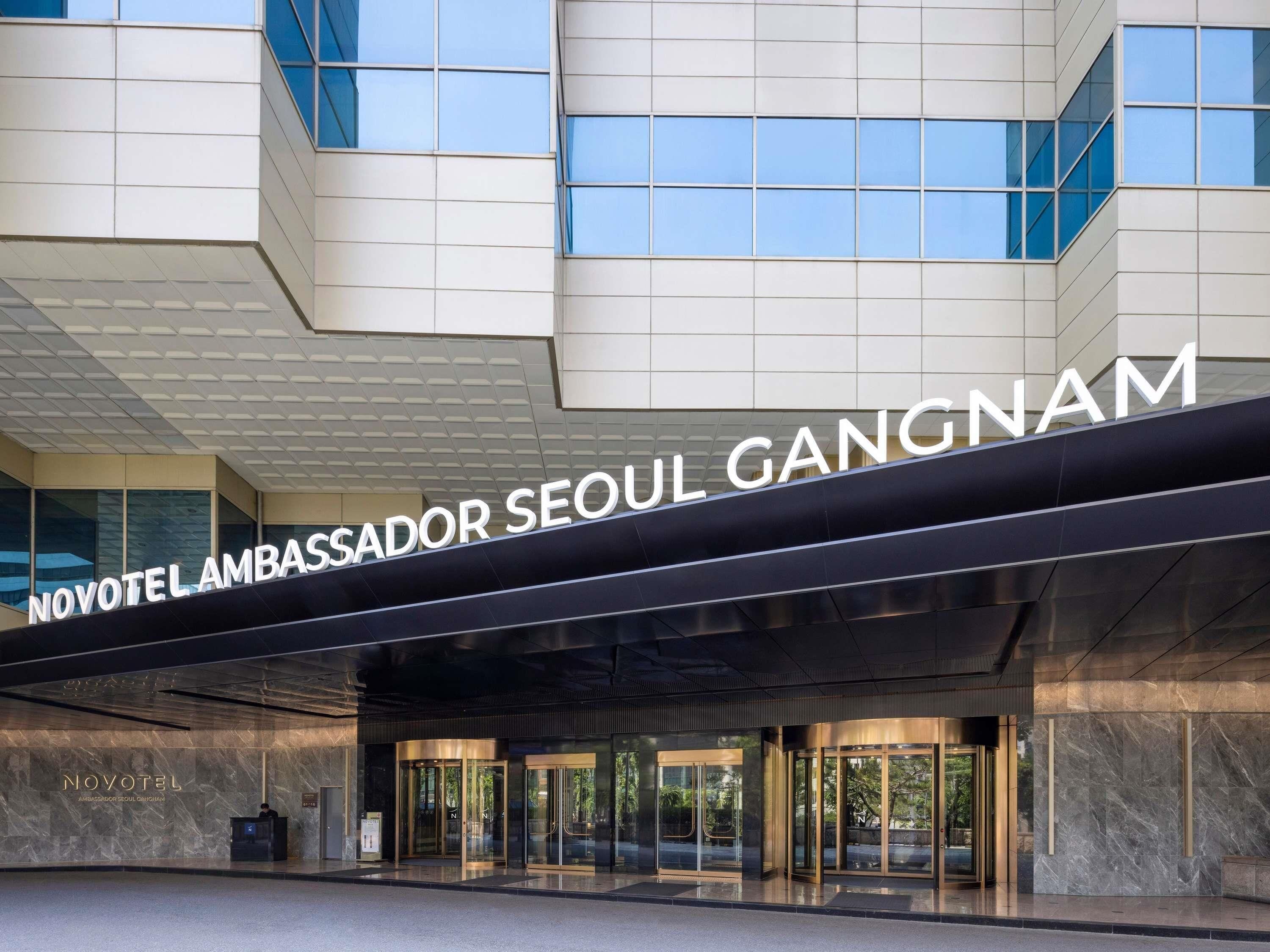 A modern hotel entrance with a prominent sign reading 'NOVOTEL LAMBASSADOR SEOUL GANGNAM.'
