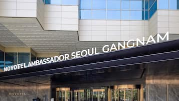 A modern hotel entrance with a prominent sign reading 'NOVOTEL LAMBASSADOR SEOUL GANGNAM.'