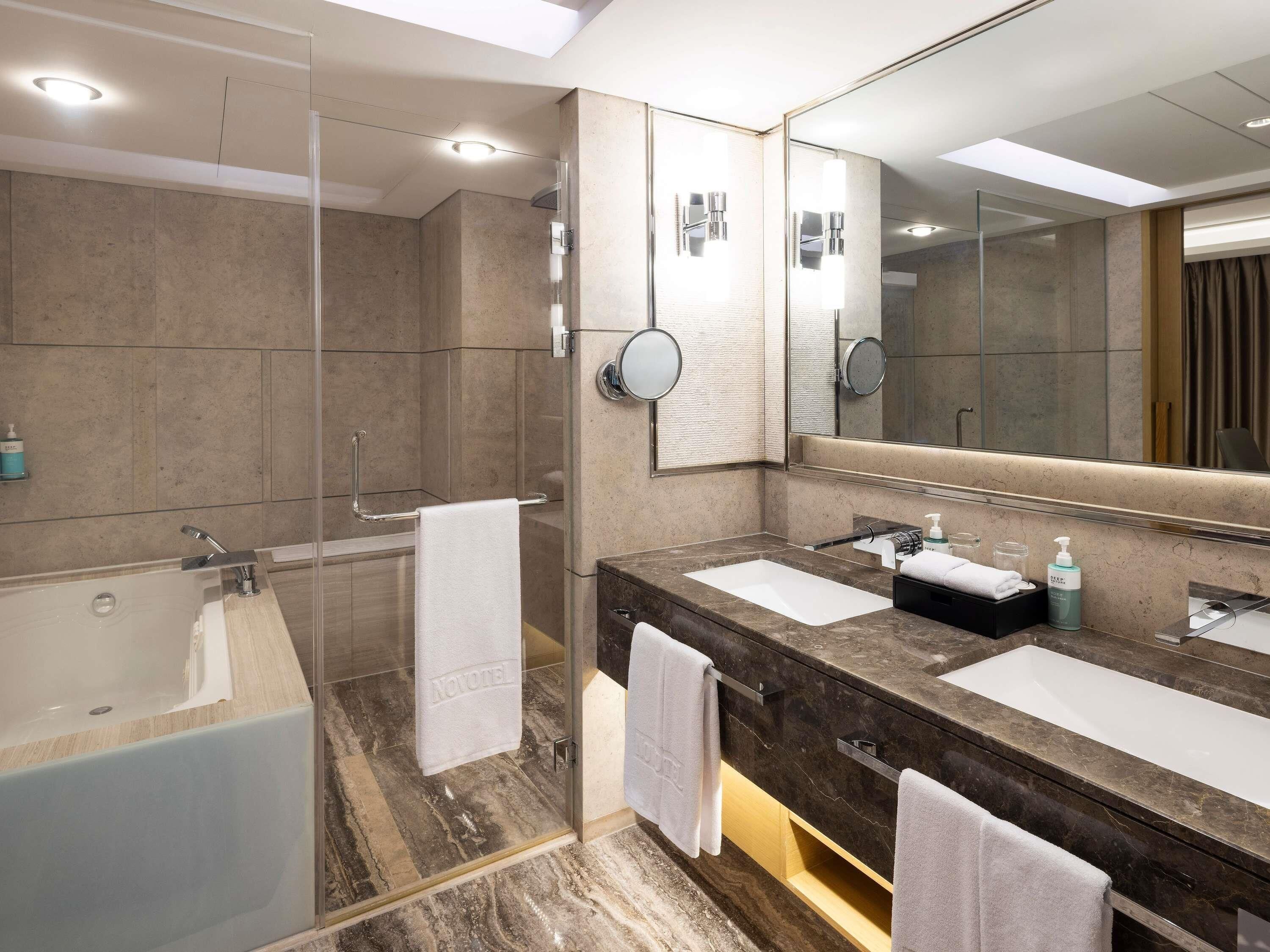 Ein modernes Badezimmer mit einer Glaskabine zur Dusche, zwei Waschbecken und einem großen Spiegel.