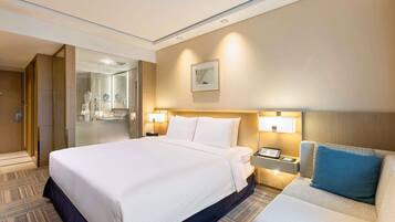 Quarto de hotel com uma cama grande, mesa de cabeceira, abajur e um sofá.