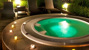 Een hottub omringd door lounge stoelen en kaarsen op een terras.