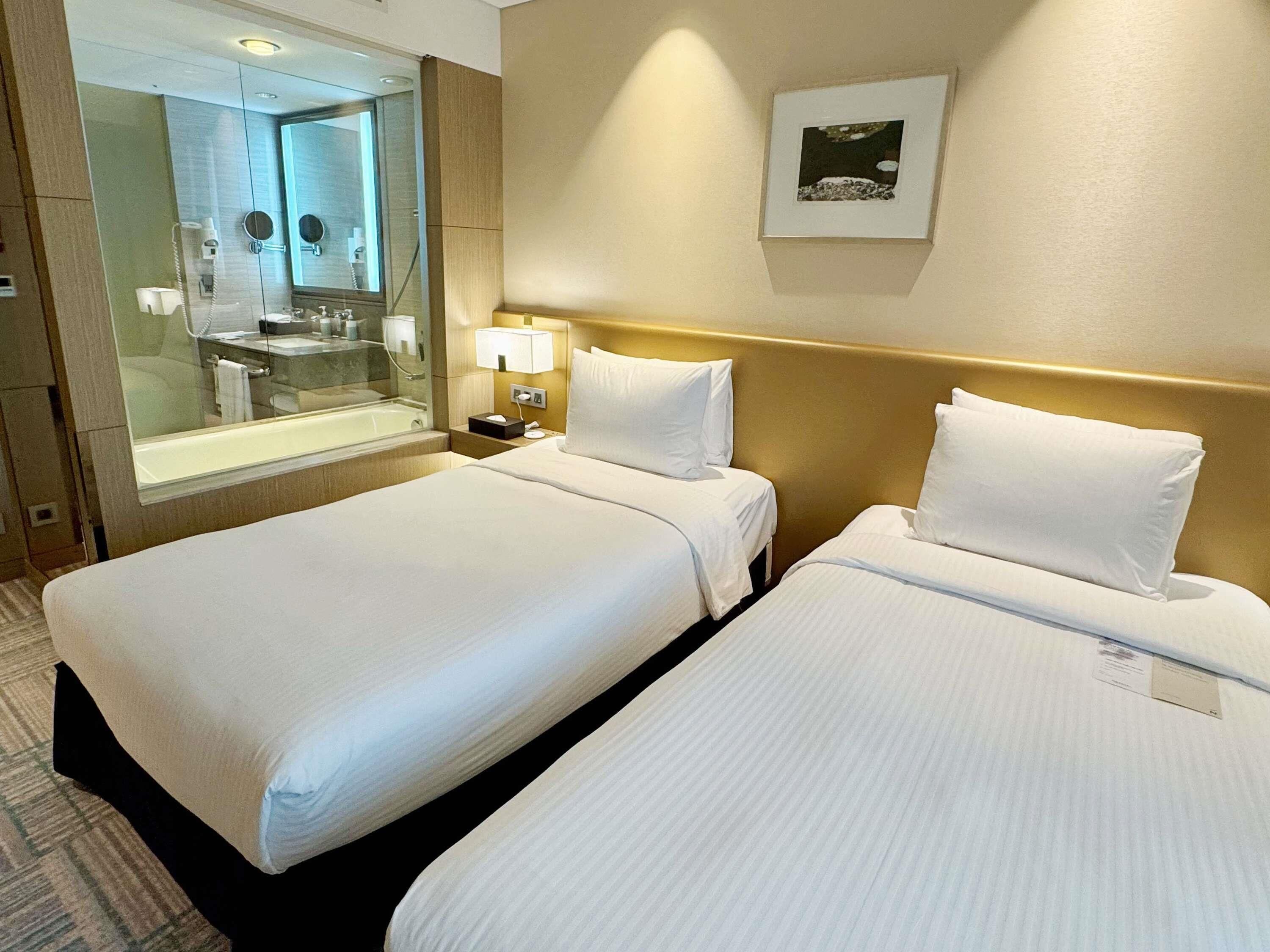 A hotel room with two beds, a bathroom with a mirror, and a framed picture on the wall.