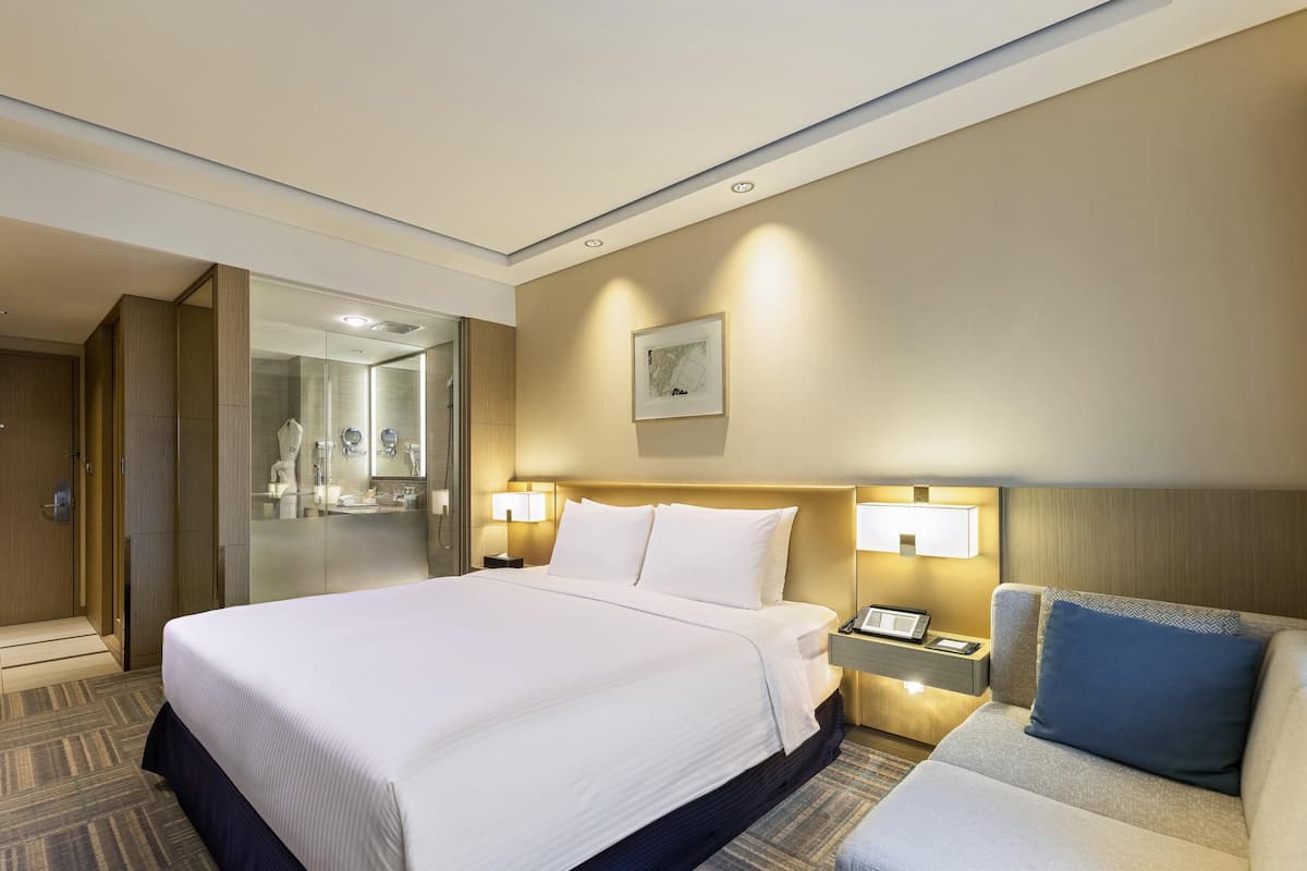 A hotel room with a large bed, bedside tables, a desk, a chair, a shower, and a bathroom with a mirror.