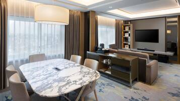 A modern hotel room with a marble dining table, comfortable seating, a sofa, a flat-screen TV, and a minibar.