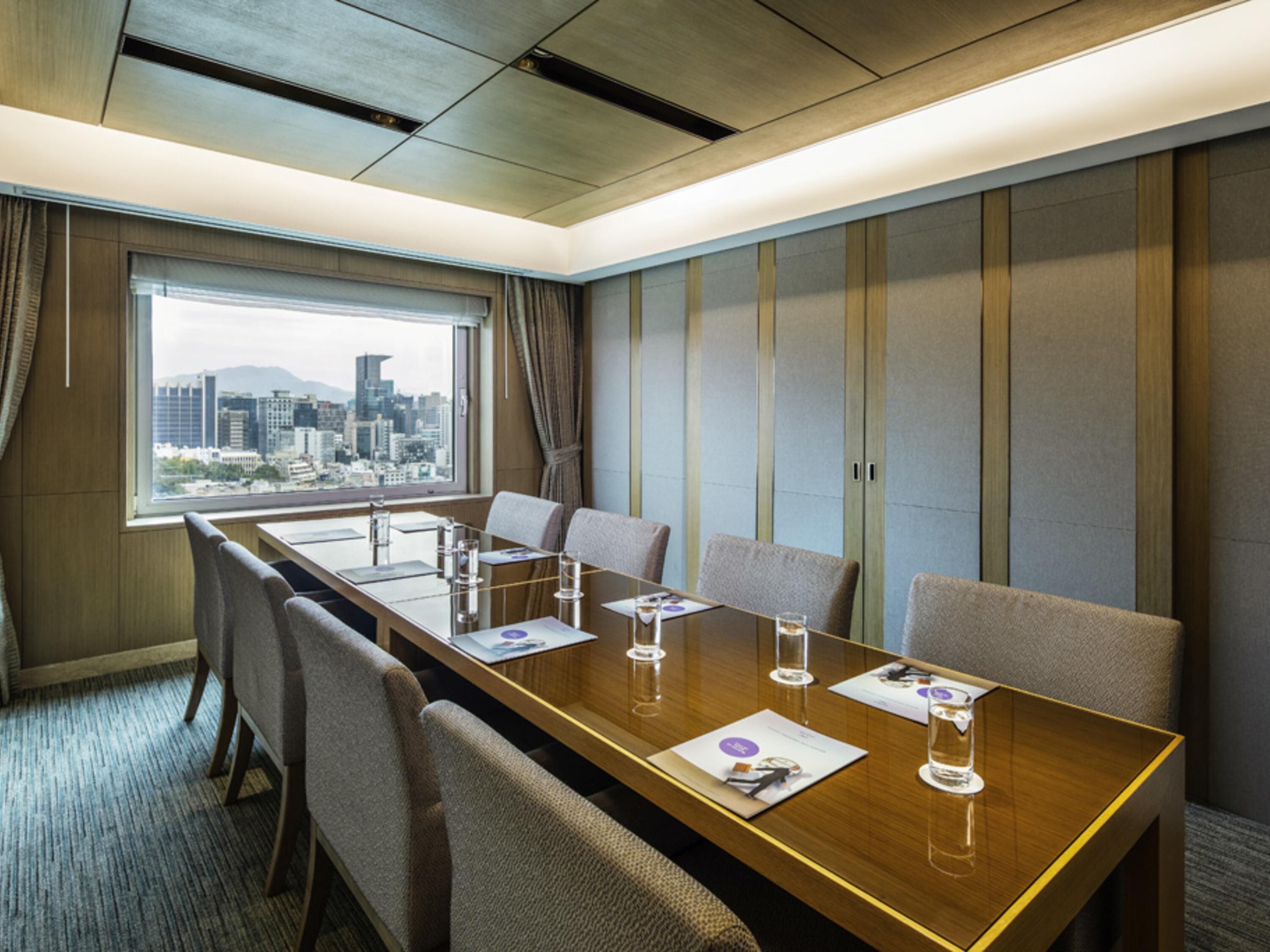 A conference room with a long table, chairs, and a city view through the window.