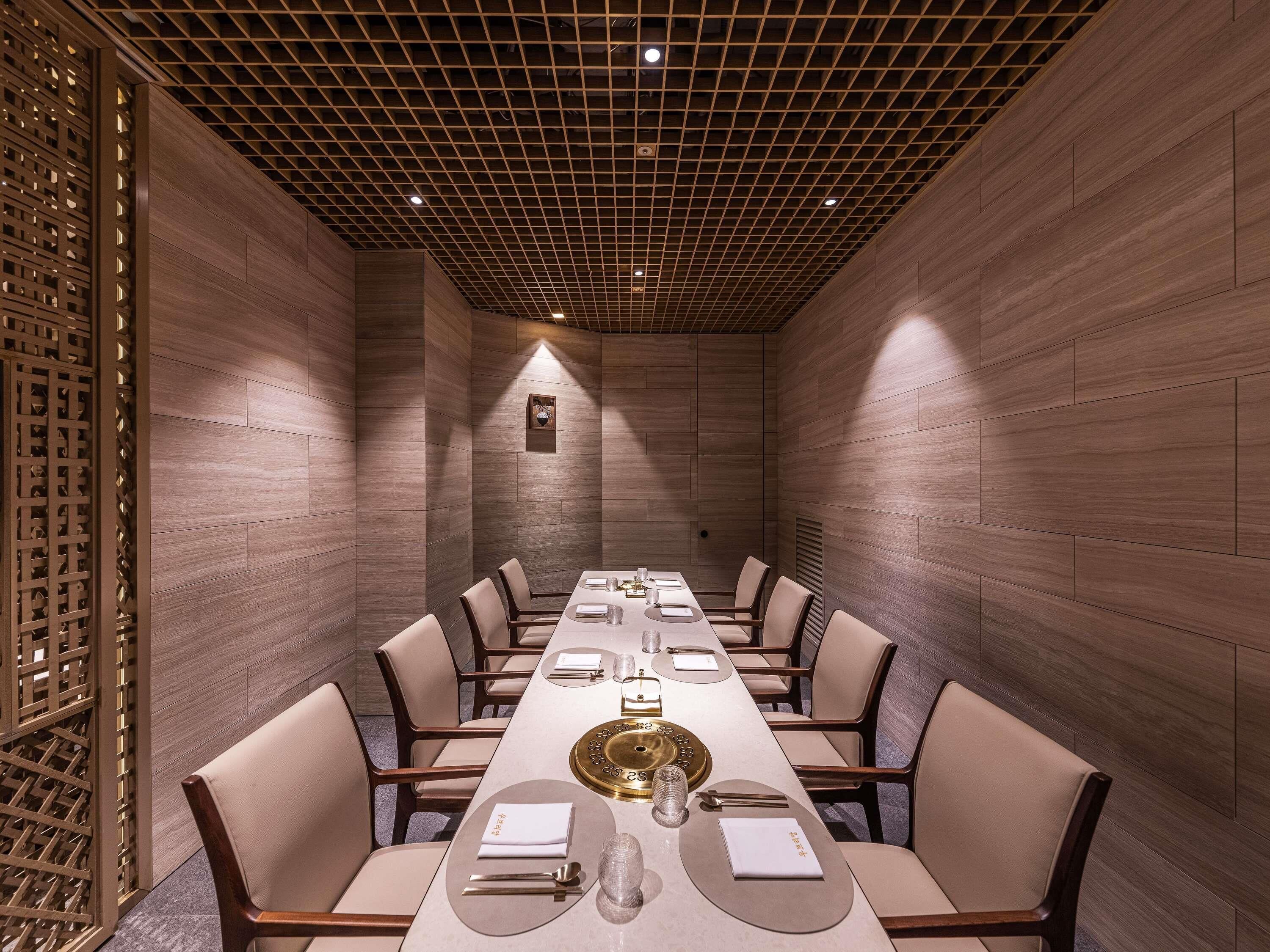 Un salón de conferencias con una larga mesa dispuesta para una reunión, paredes de paneles de madera y un techo con diseño de cuadrícula.