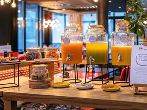 Un bufé de desayuno con diversas opciones de comida y dos dispensadores de jugo de naranja.