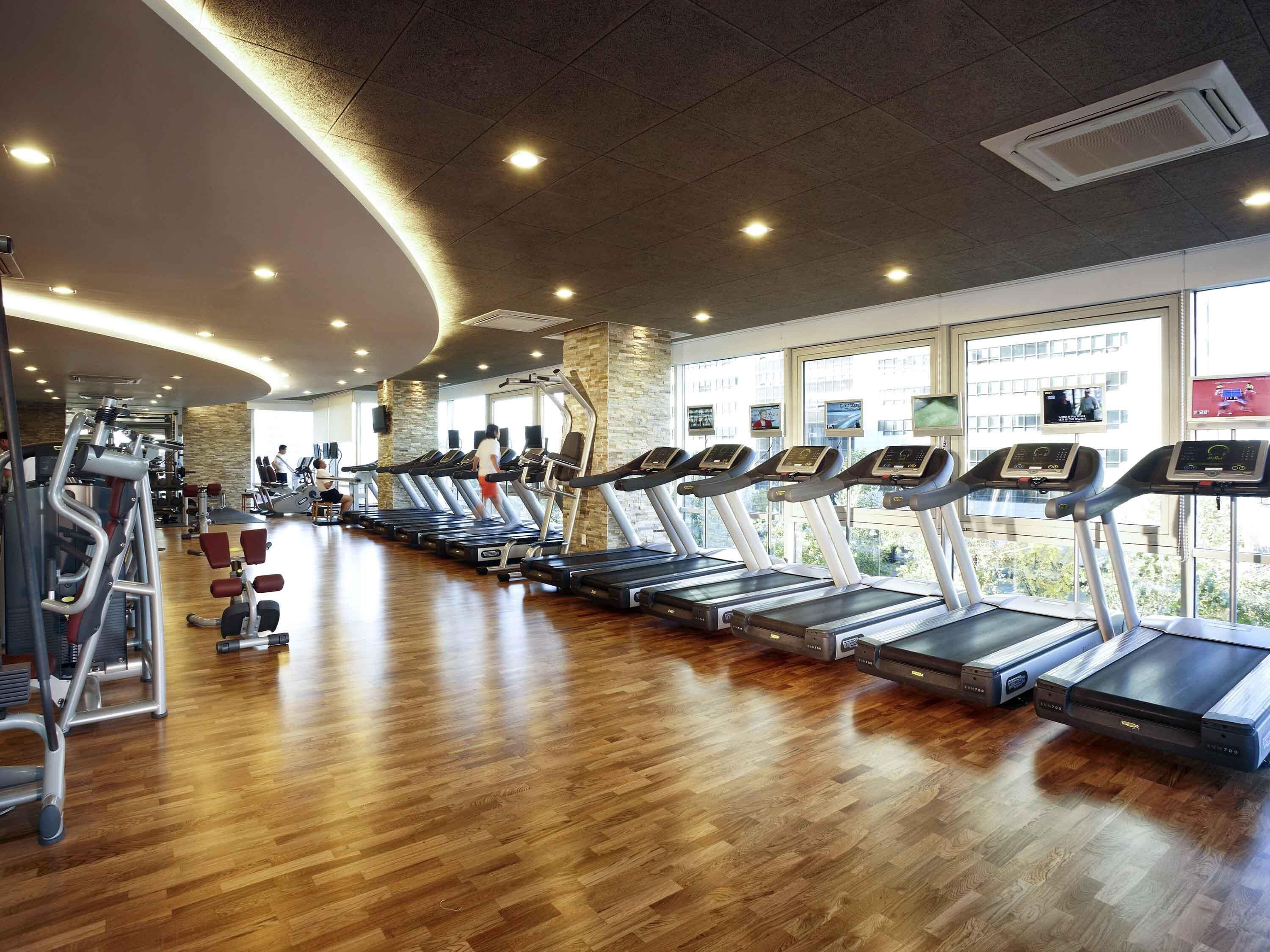 A gym with treadmills, weight machines, and a wooden floor.
