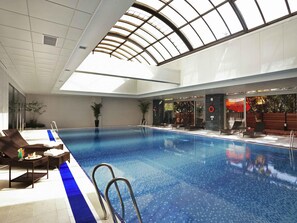Una piscina interior con sillones de descanso, tragaluz y vistas al exterior.