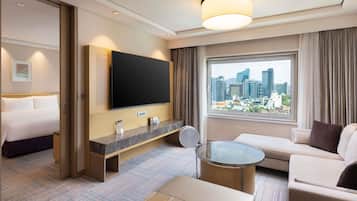 Quarto de hotel com cama, televisão, sofá, mesa de centro e janela com vista para a cidade.