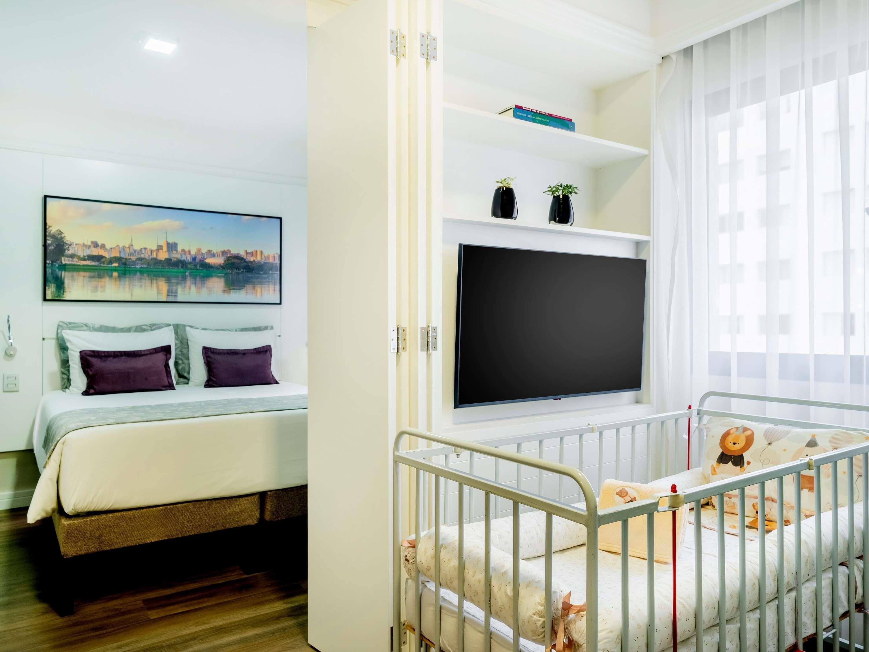 Un dormitorio con una cama, televisor, cuna y un cuadro en la pared.