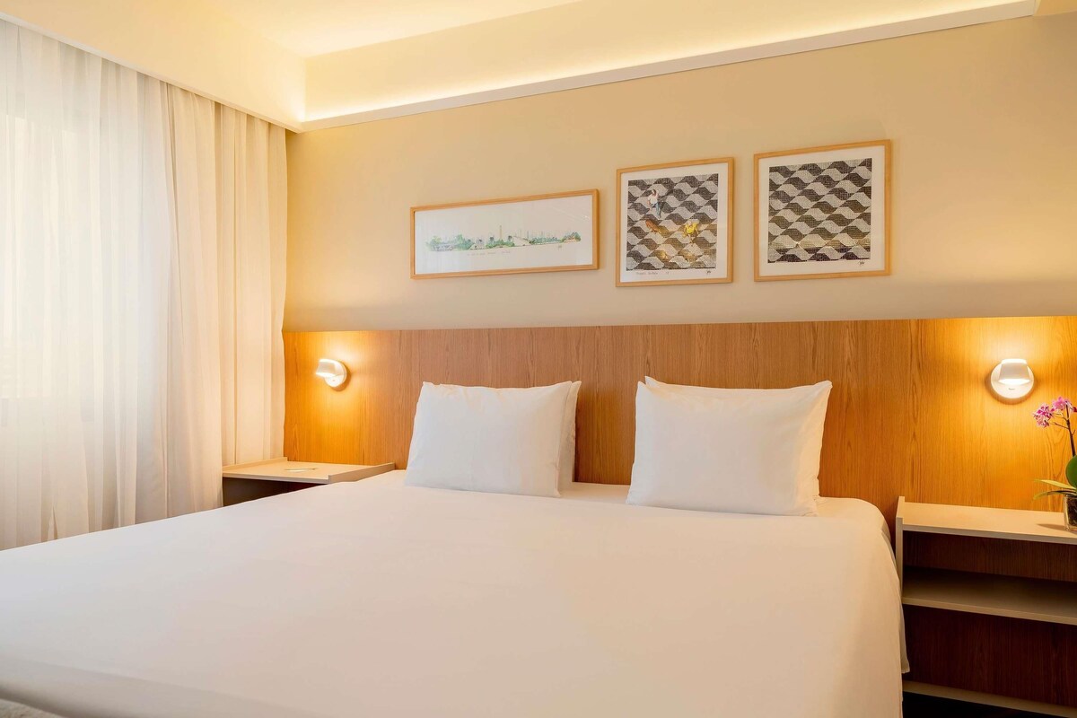 A hotel room with a large bed, two bedside tables, and three framed pictures on the wall.