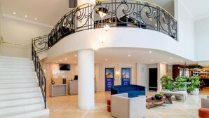 Un hall d’entrée spacieux avec un escalier en courbe, un comptoir d’accueil, un espace salon et une grande plante en pot.