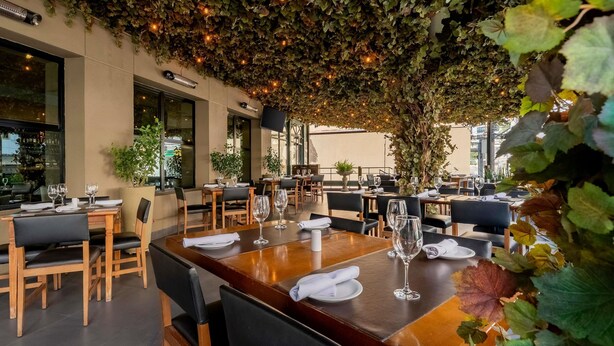 Un espace de restauration en plein air, avec des tables et des chaises, entouré de verdure et illuminé de guirlandes lumineuses.