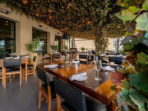 An outdoor dining area with tables and chairs, surrounded by greenery and string lights.