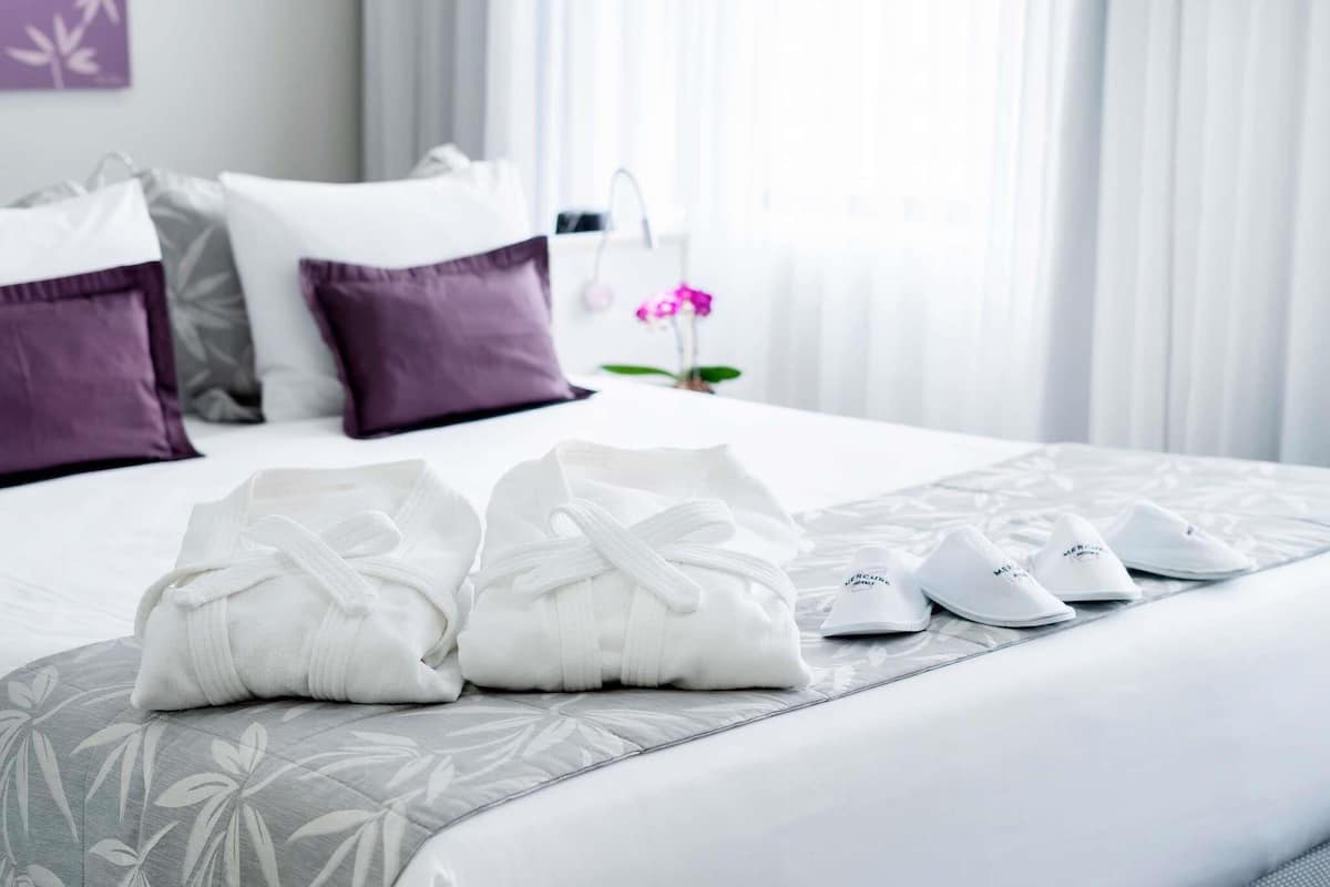 Ein ordentlich bezogenes Bett mit Kissen, einer Bettdecke mit Blumenmuster und einem Paar weiße Schuhe darauf.