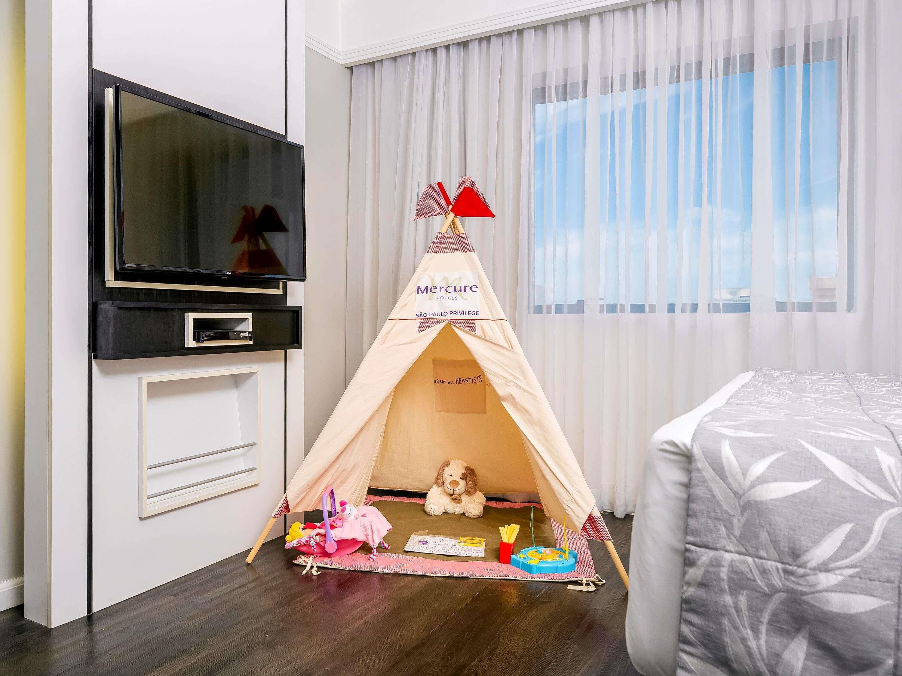 A hotel room with a TV, a tent, a bed, and a window with curtains.