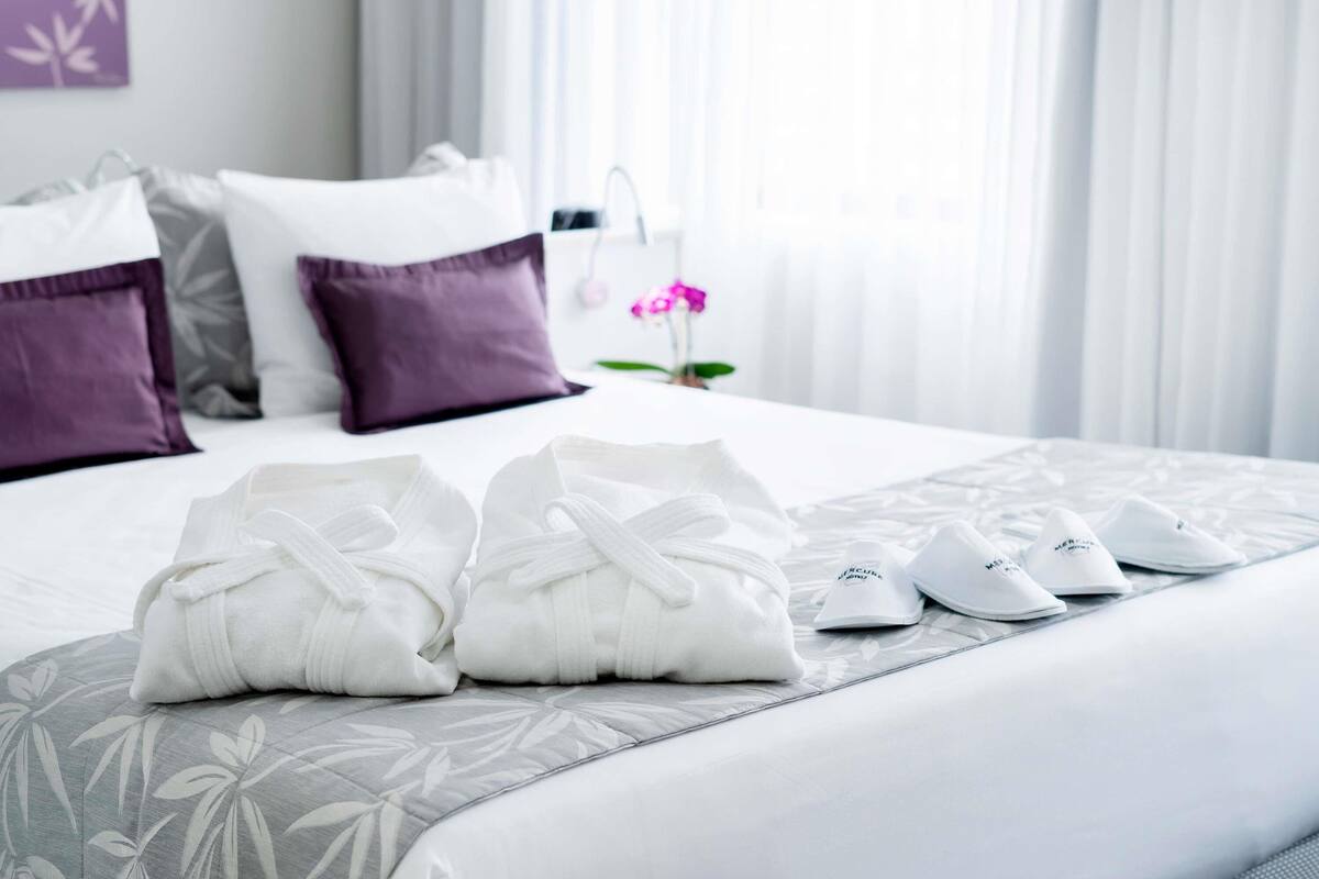 Una cama bien hecha con almohadas, una manta y un par de zapatos sobre la cama.
