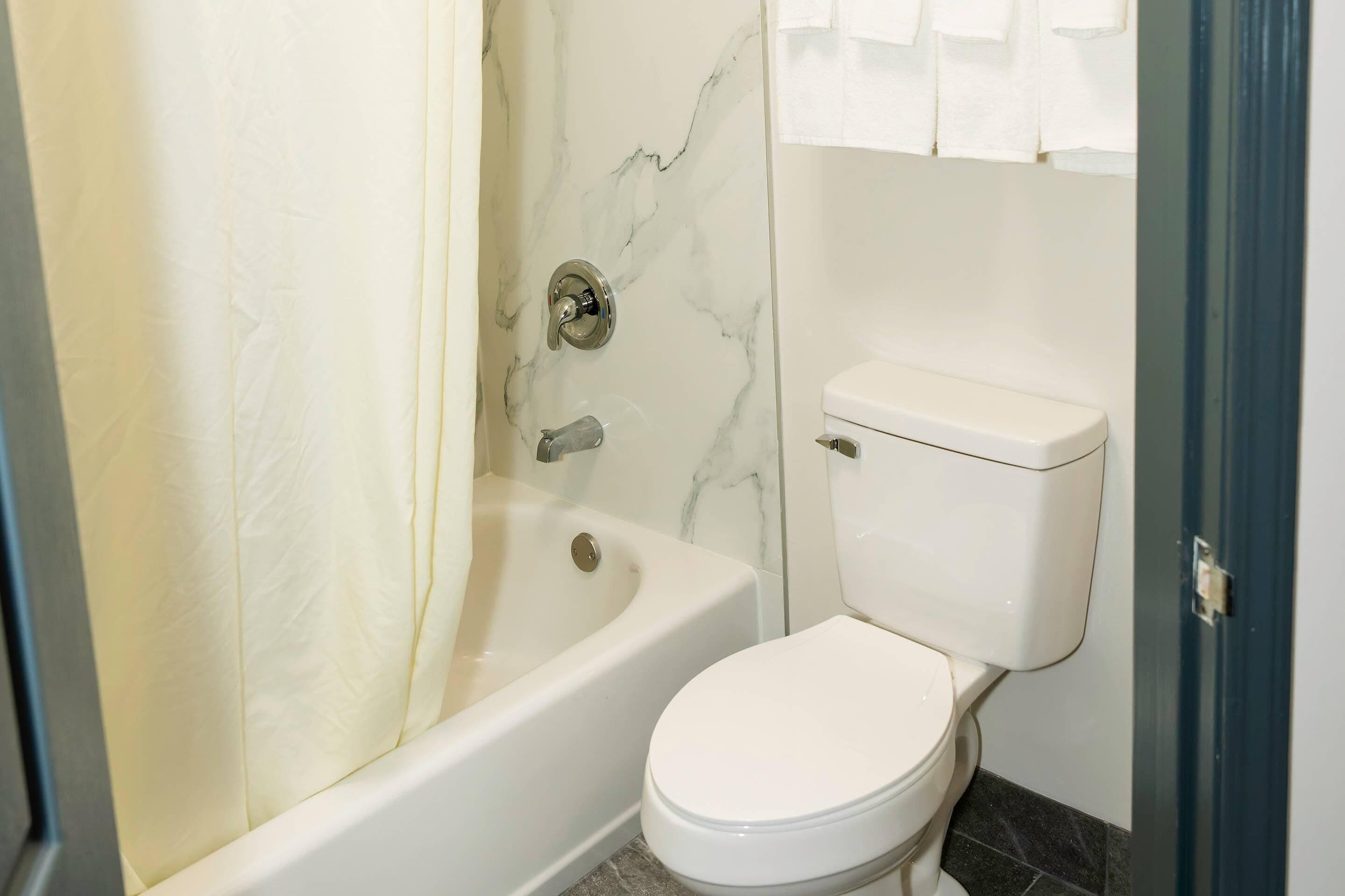 A bathroom with a bathtub, toilet, and marble walls.