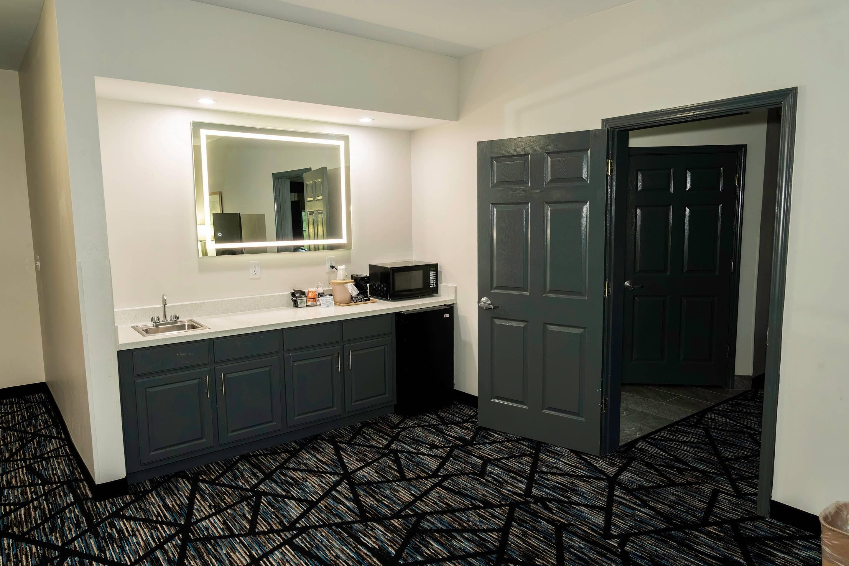 A modern bathroom with a large mirror, a sink, a microwave, and a dark door.