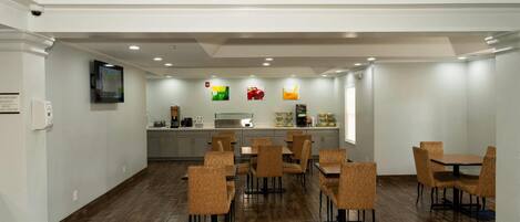 A spacious dining area with wooden flooring and wicker chairs, a kitchen area with a stainless steel refrigerator, and a flat-screen TV mounted on the wall.