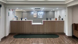 A hotel reception area with a modern design, featuring a reception desk, a digital check-in kiosk, and a sign indicating 'Quality by Choice Hotels'.