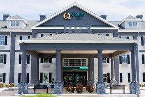 Entrada de un hotel con un porche cubierto, columnas y un letrero que dice 'Quality Inn'.