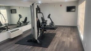 Un gimnasio con máquinas de cardio, un espejo grande y un televisor de pantalla plana.