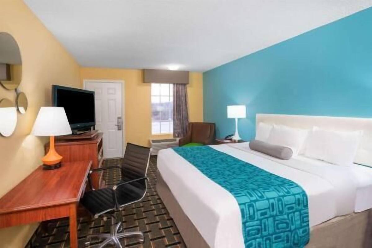 A hotel room with a bed, a desk, a chair, a television, and a window.