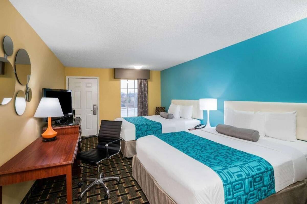 A hotel room with two beds, a desk, a chair, a TV, and a window.