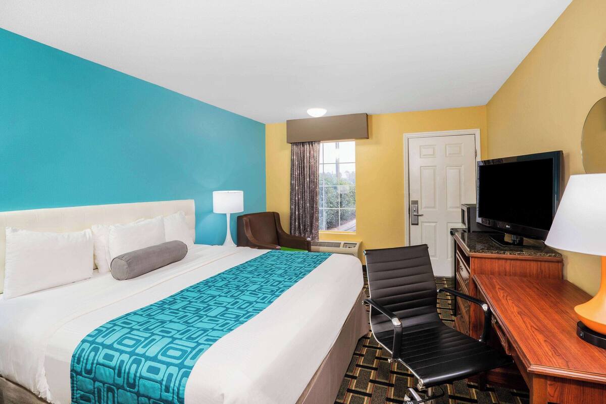 A hotel room with a bed, a desk with a television, a chair, and a window with curtains.