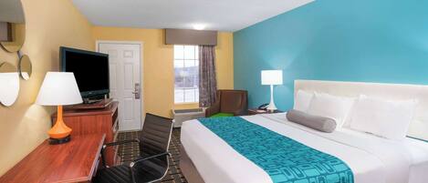 A hotel room with a bed, desk, chair, TV, and two lamps.
