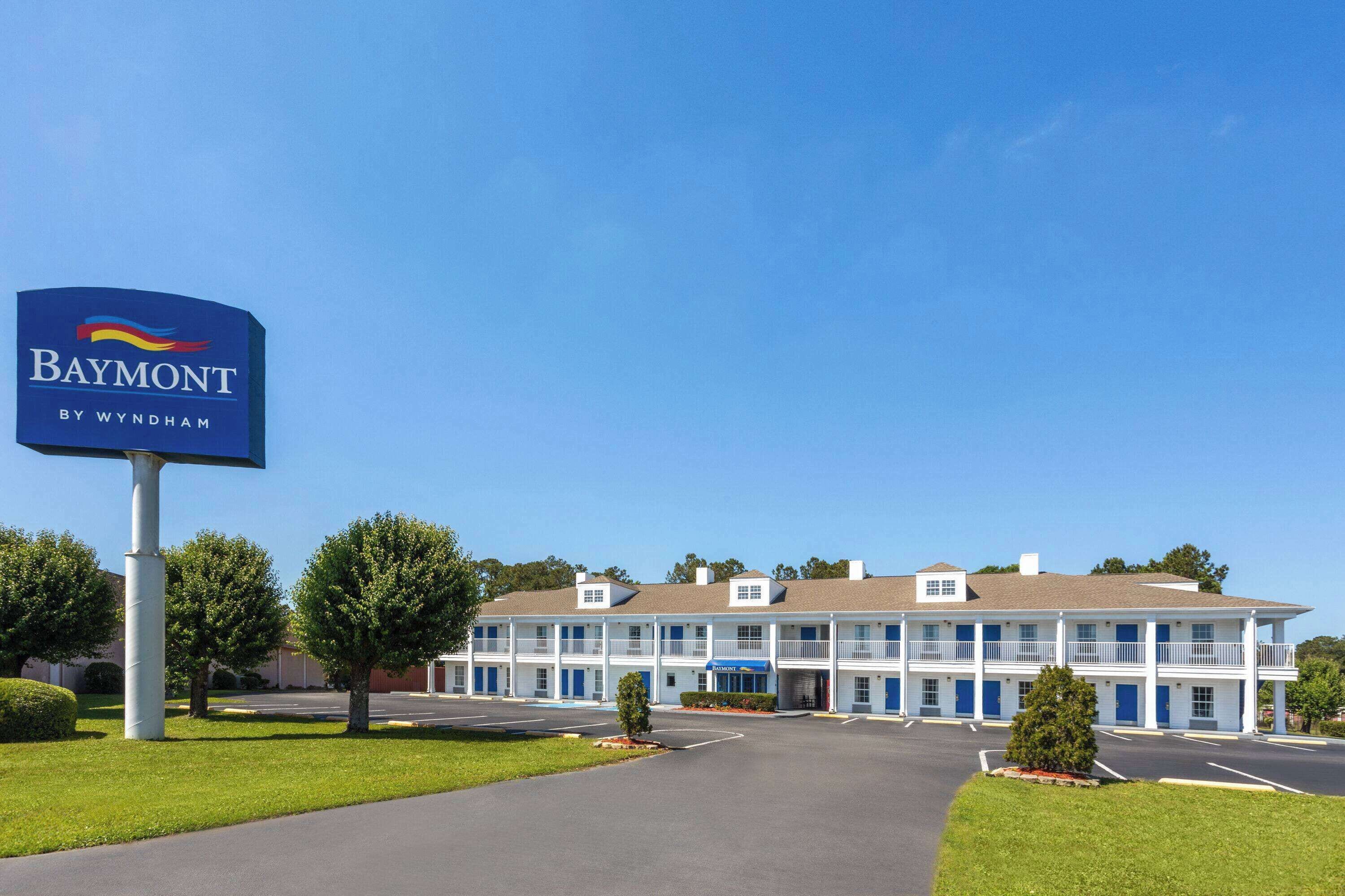 Um hotel Baymont by Wyndham com estrutura de dois andares, estacionamento e céu azul límpido.
