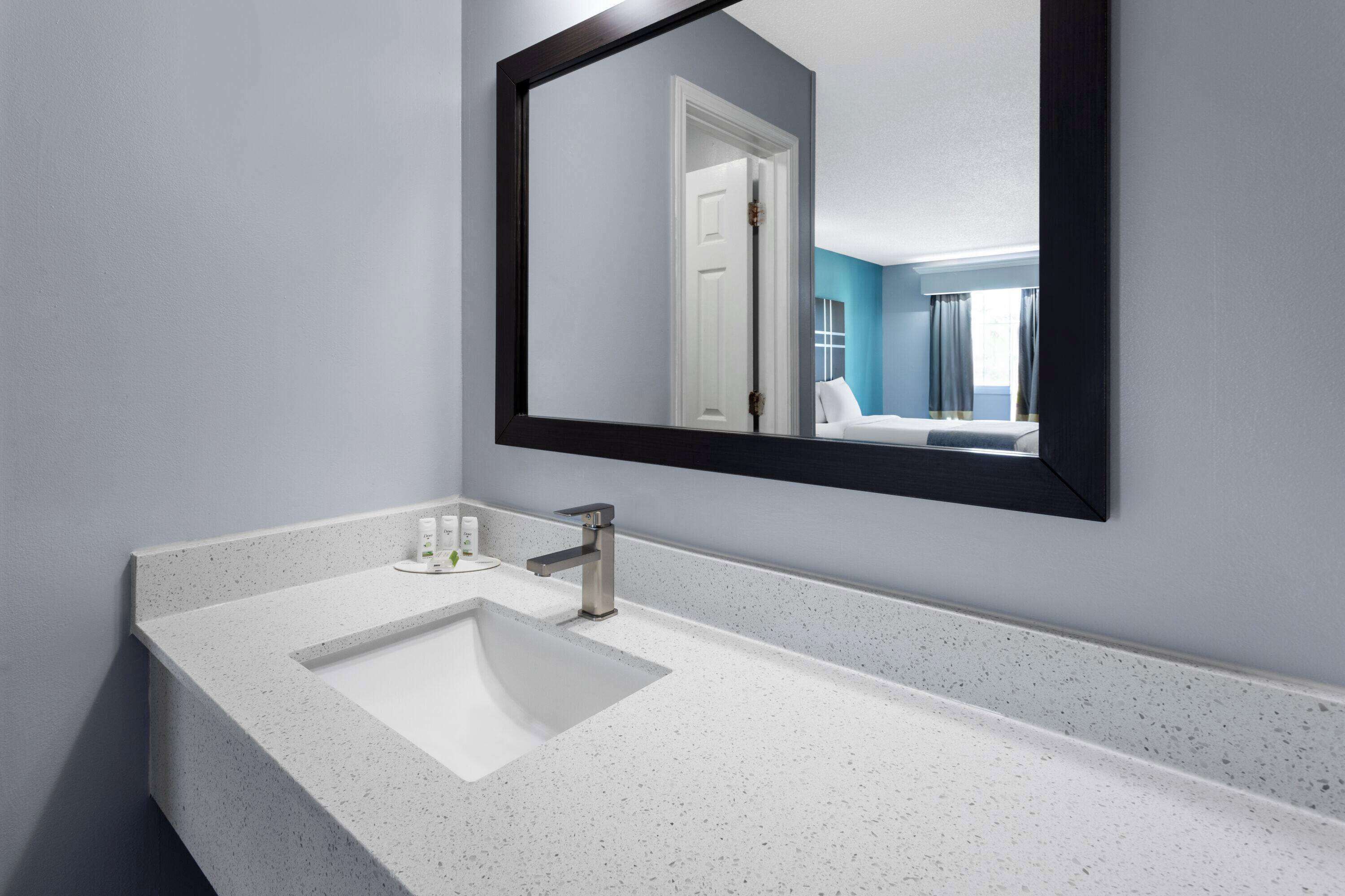 Een moderne badkamer met een witte, gespikkelde wastafel, een enkele wasbak en een grote spiegel.