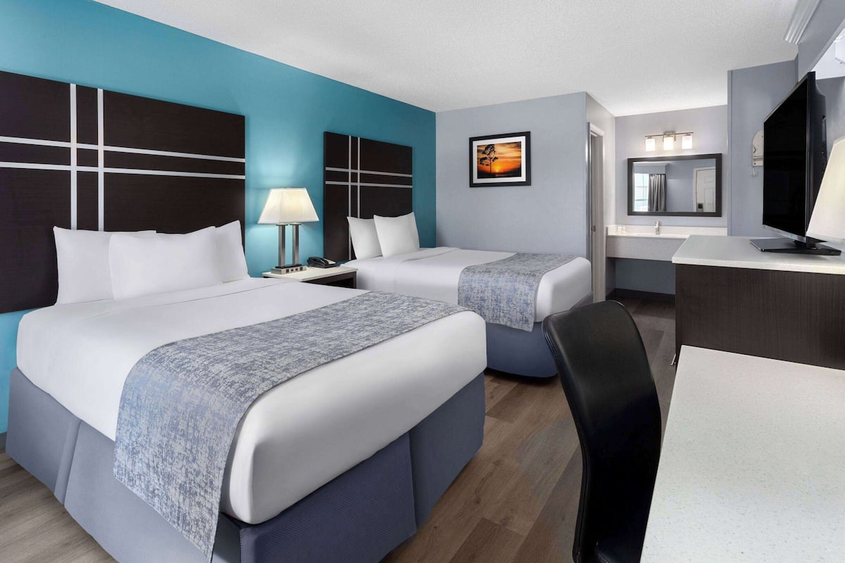 A hotel room with two beds, a desk, a TV, and a bathroom with a mirror and lights.