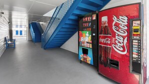 A Coca-Cola vending machine in a modern building with a blue staircase and a bench.