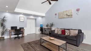 A spacious living room with a dark gray sofa, a wooden coffee table, and a desk with a computer.