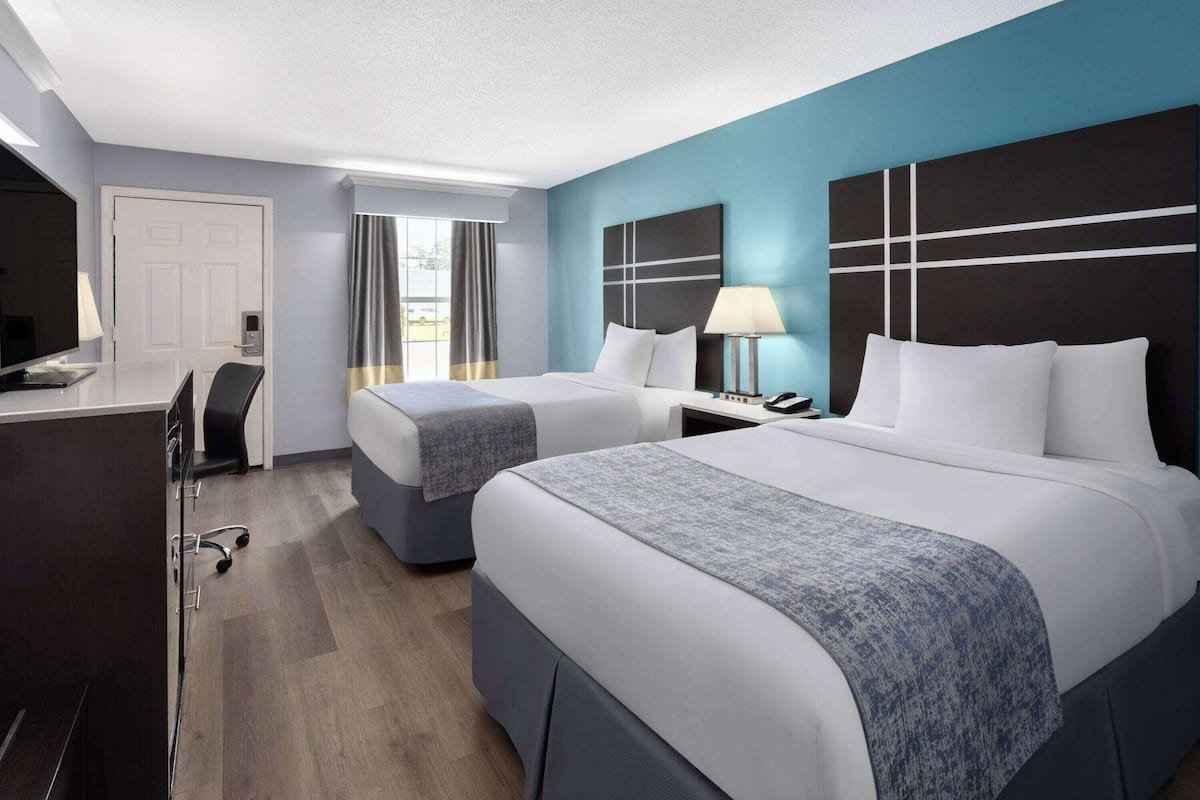 A hotel room with two beds, a desk, a chair, a TV, and a window with curtains.