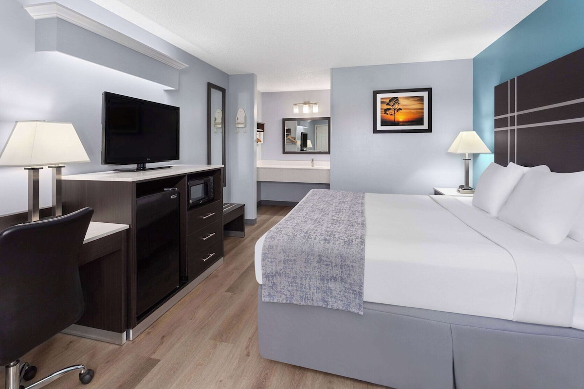 A modern hotel room with a bed, desk, television, and a bathroom visible in the background.