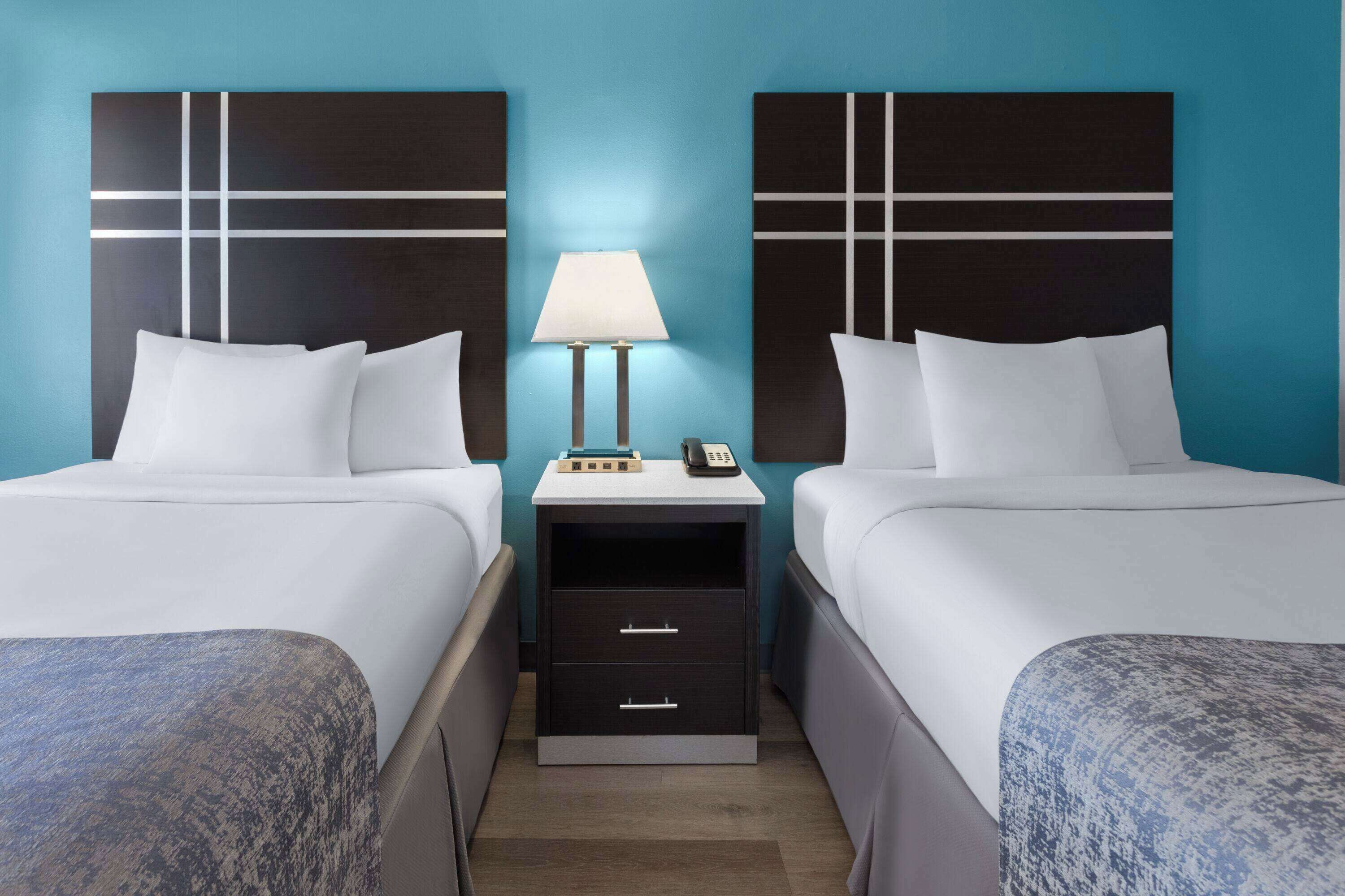 A hotel room with two beds, a nightstand with a lamp, and a phone.