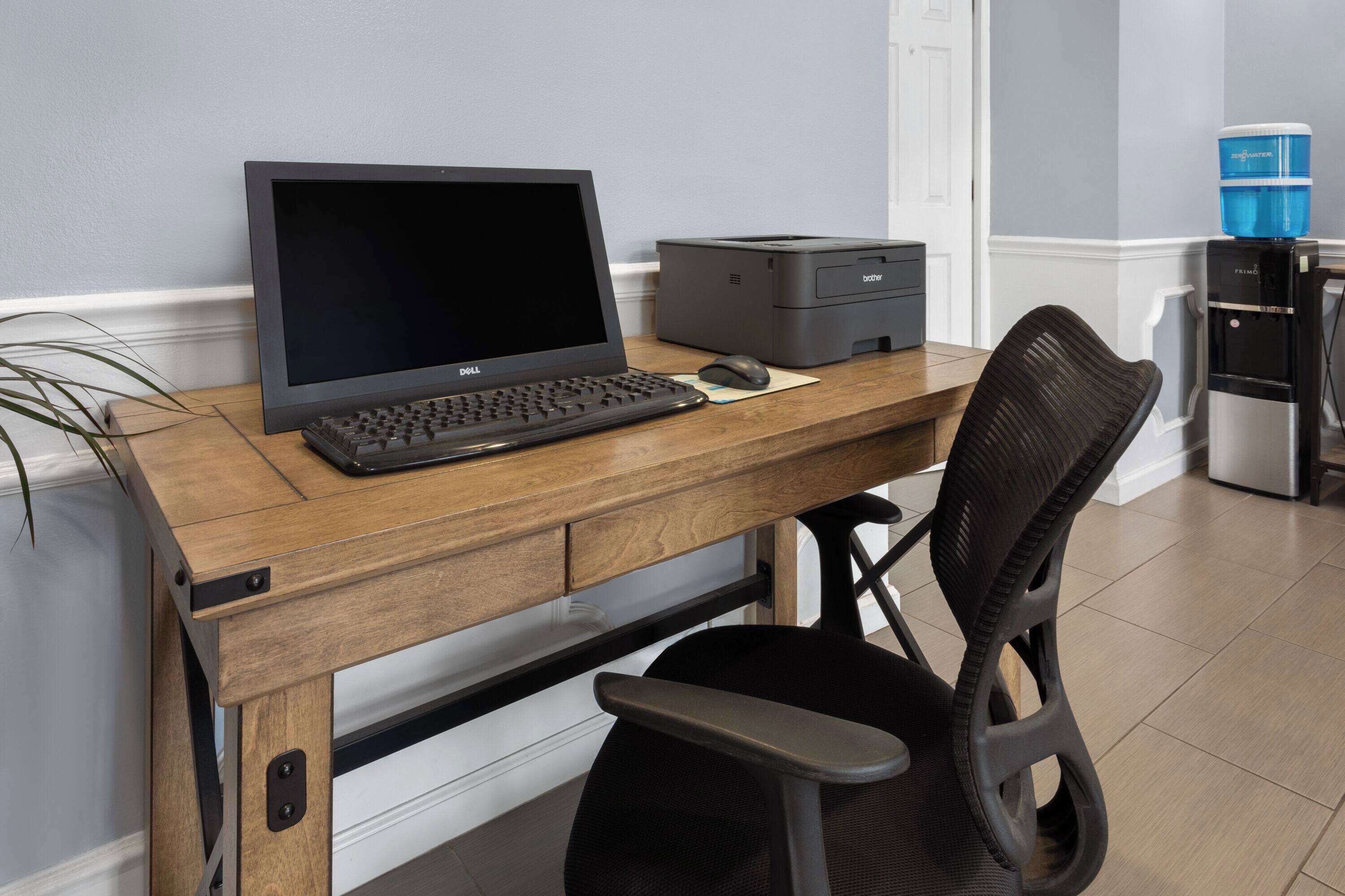 A wooden desk with a Dell laptop, a printer, and a black office chair.
