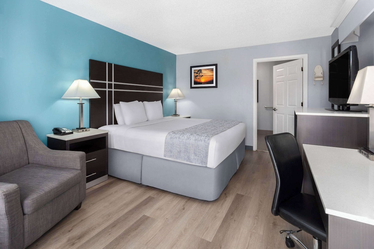 A modern hotel room with a bed, bedside tables, a desk, and a chair.