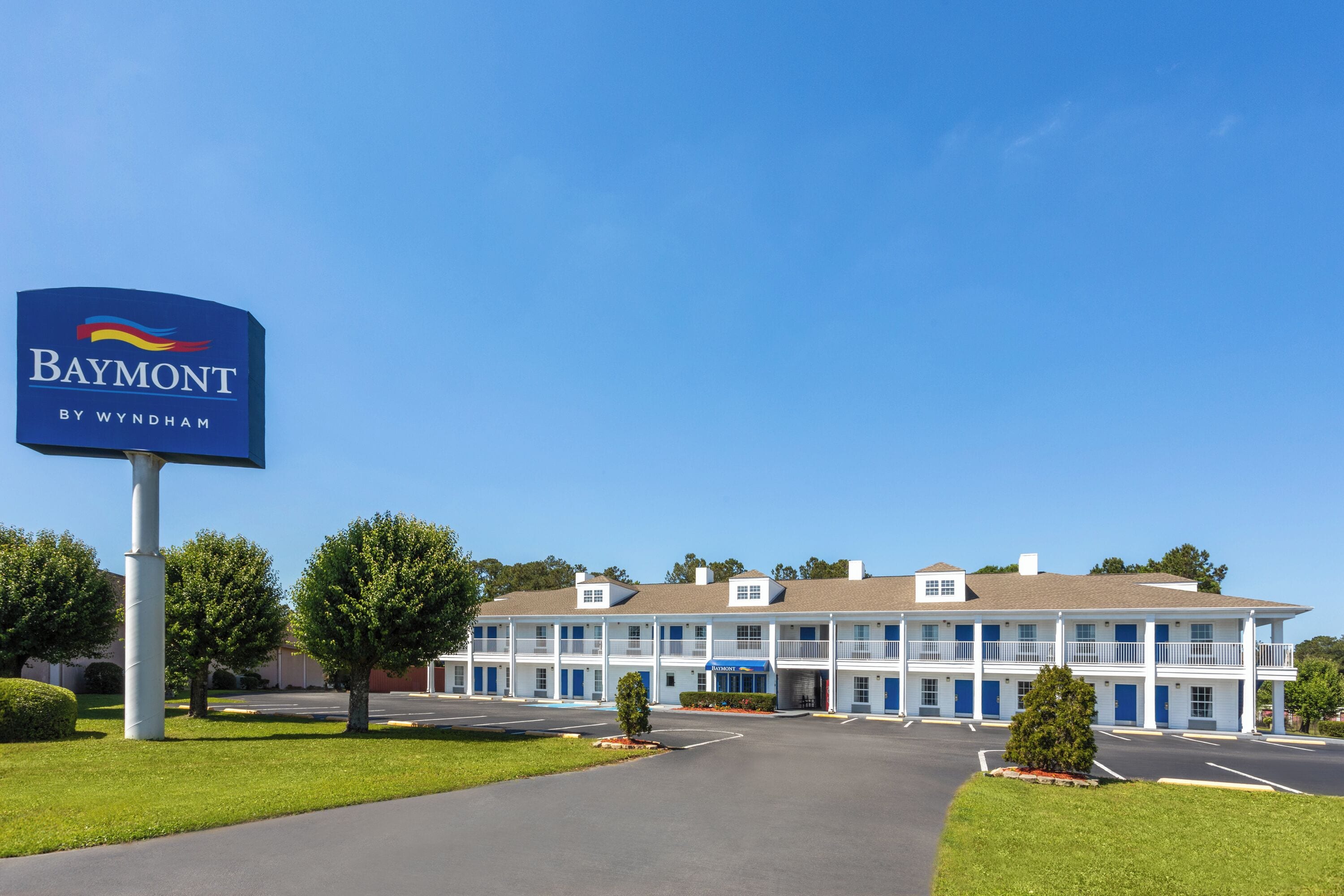 A Baymont by Wyndham hotel with a two-story structure, a parking lot, and a clear blue sky.