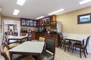 Una cocina con armarios de madera, un refrigerador y un microondas. Hay dos mesas de comedor con sillas.