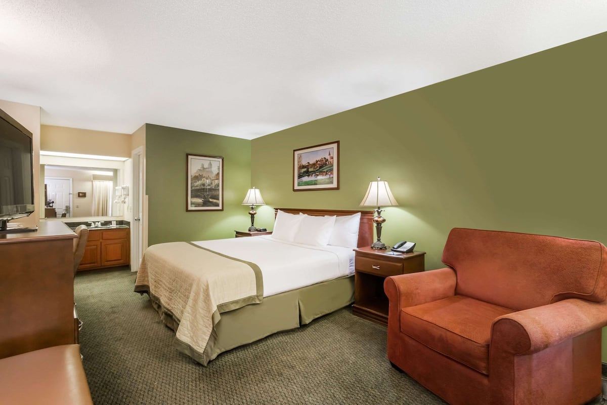 A hotel room with a bed, two bedside lamps, a chair, a desk, and a television.