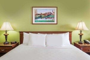 Una habitación de hotel con una cama, dos mesitas de noche con lámparas, un cuadro enmarcado en la pared y una pared verde.