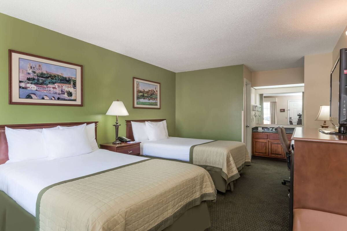 A hotel room with two beds, a desk, a chair, a TV, and a bathroom visible through an open door.